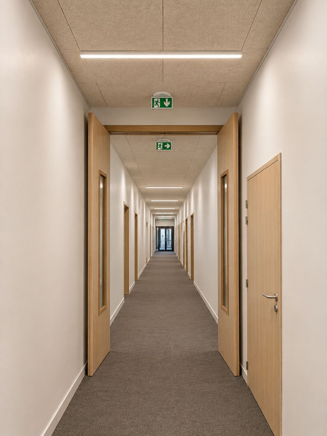 Couloir équipé de blocs-portes en menuiserie intérieure avec châssis vitrés et issues de secours